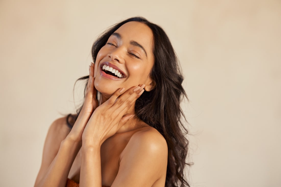 A woman smiling while touching her face